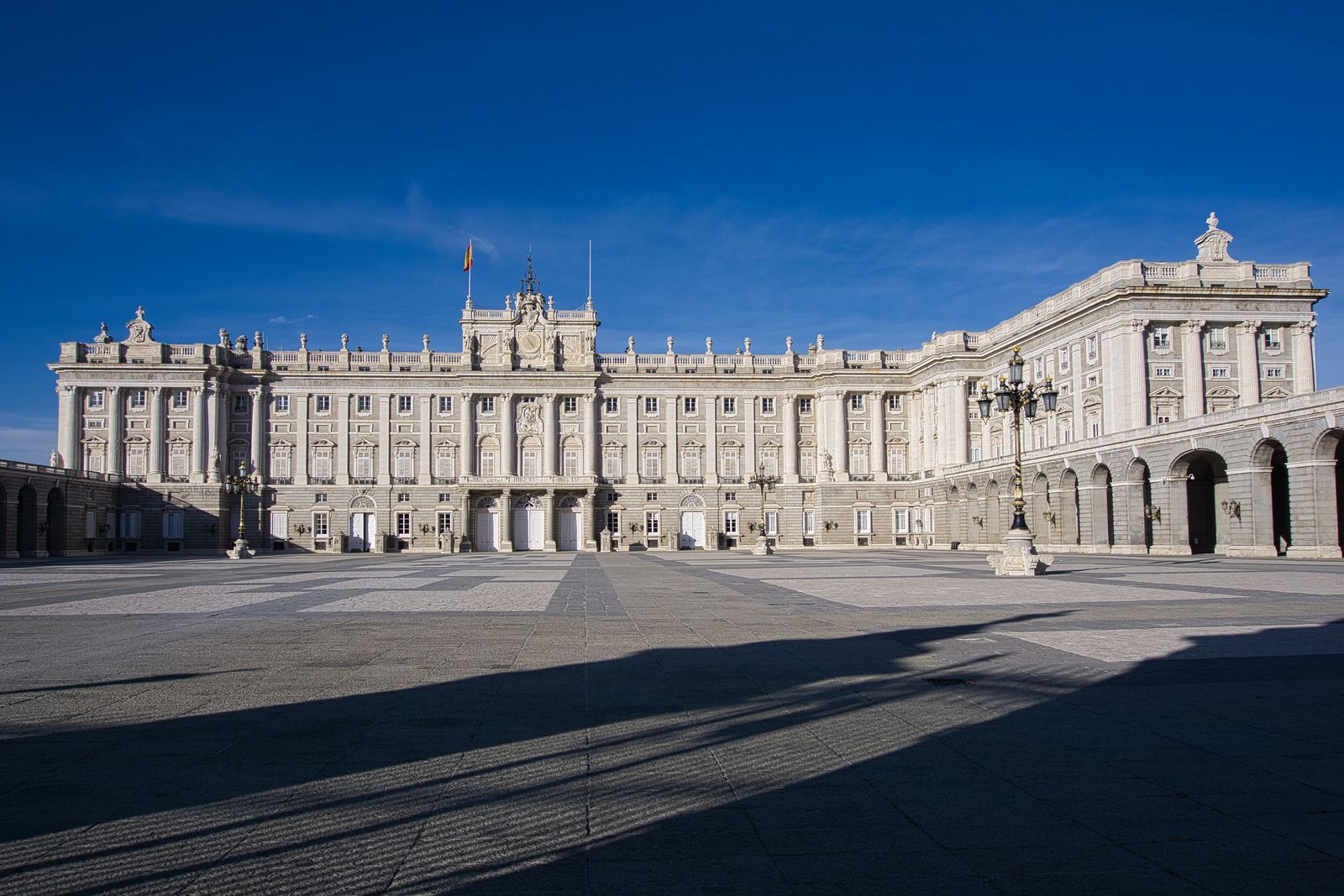 La Puerta de Alcalá de Madrid con sus arcos de piedra y parterres de flores naranjas en un día soleado